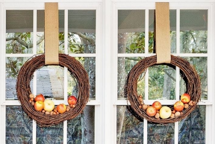 Two fall wreaths with apples hanging on windows panes. 