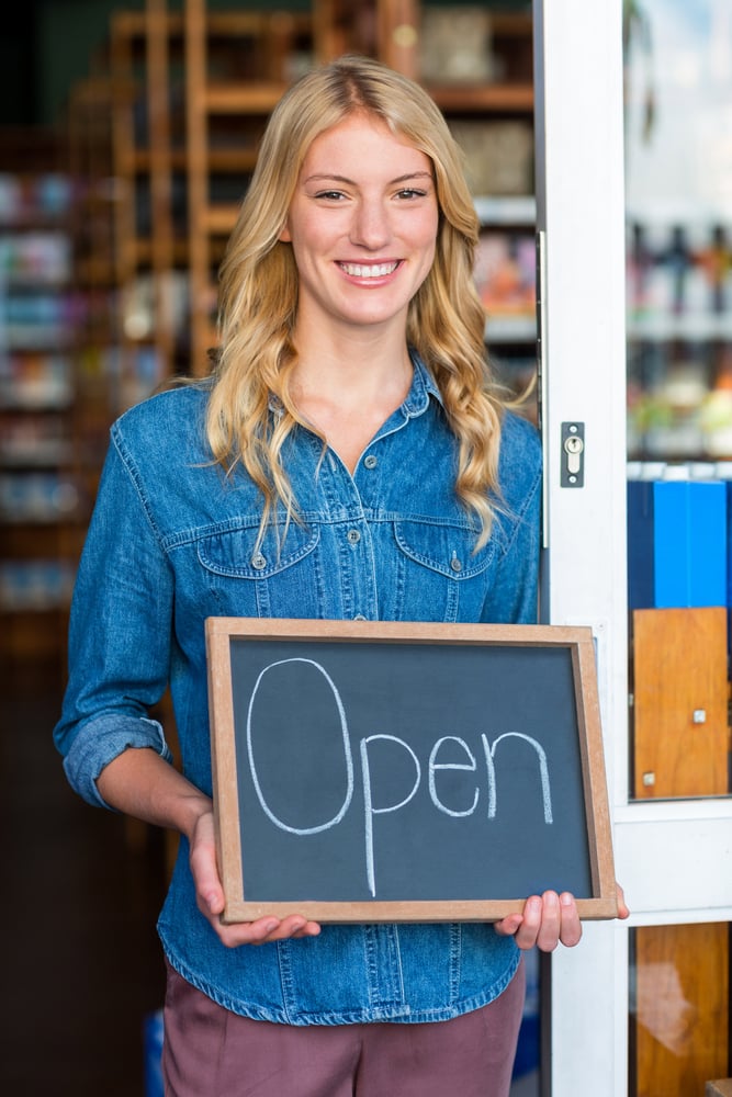 Portrait of smiling owner holding open signboard in supermarket